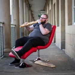 Luke Bonaccorsi sat on a red chair, eating a large baguette